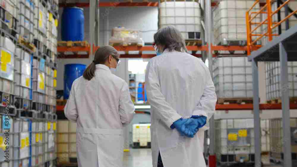 Back view of specialists in lab coat and gloves walking in industrial warehouse